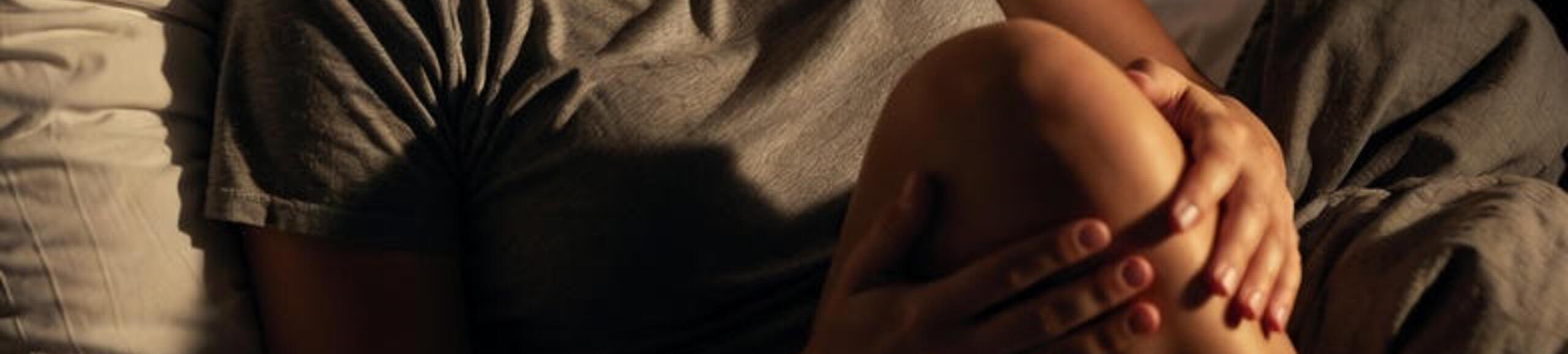 Femme allongée tenant son genou douloureux la nuit, illustrant une douleur du genou au repos ou nocturne.